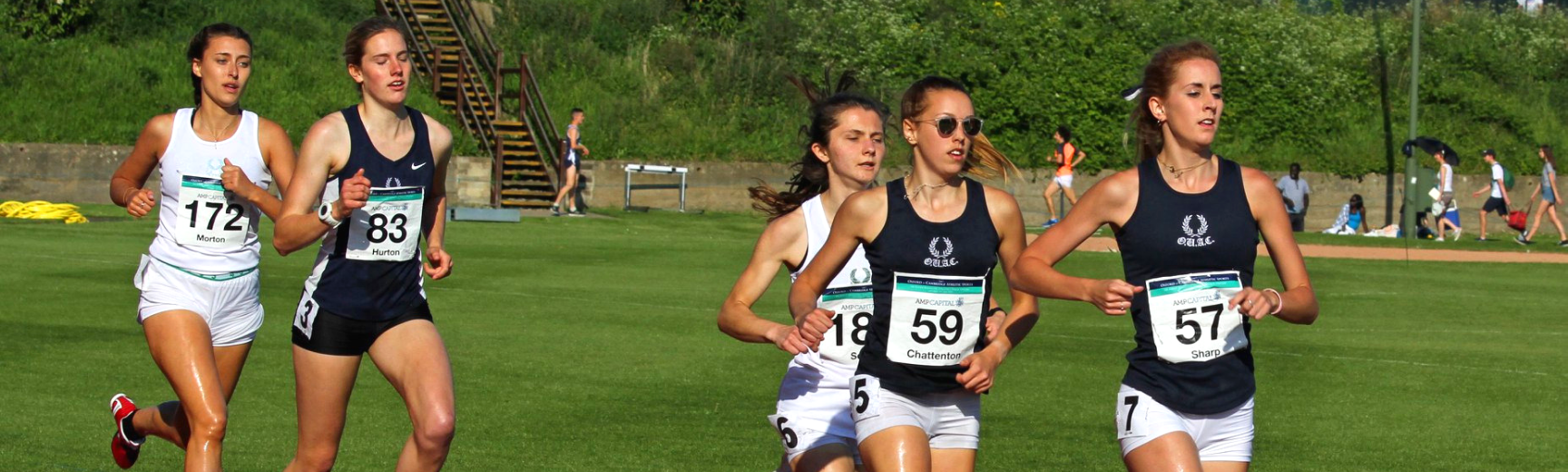 Five women running around the Sir Roger Bannisyer Running track in the Oxford vs Cambridge athletics Varsity match