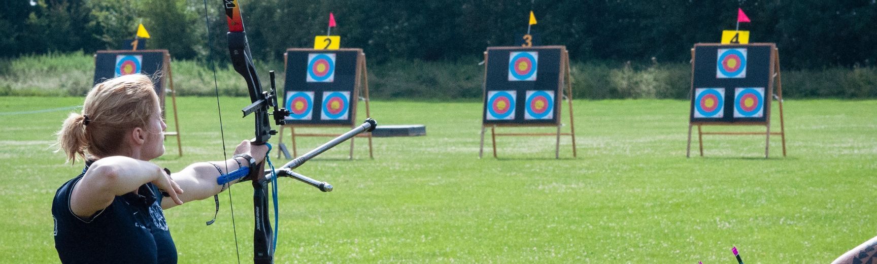 An archer with her bow pointed at a target, ready to shoot her next arrow